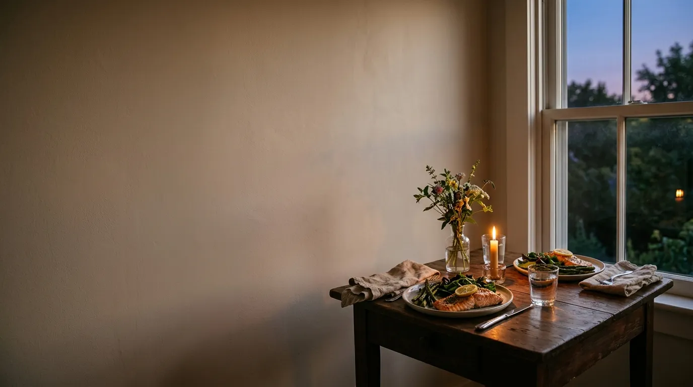 A dinner table set for two by a window at dusk