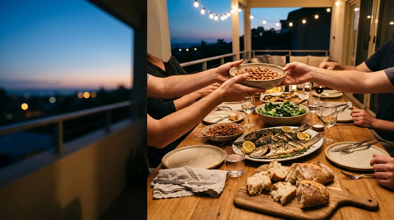 Friends sharing a meal at a long table on a terrace at dusk